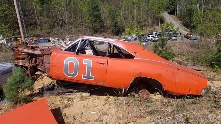 Abandoned General Lee-style Dodge Charger sitting in a junkyard, a tribute to the Dukes of Hazzard car Ben Jones' character Cooter kept running
