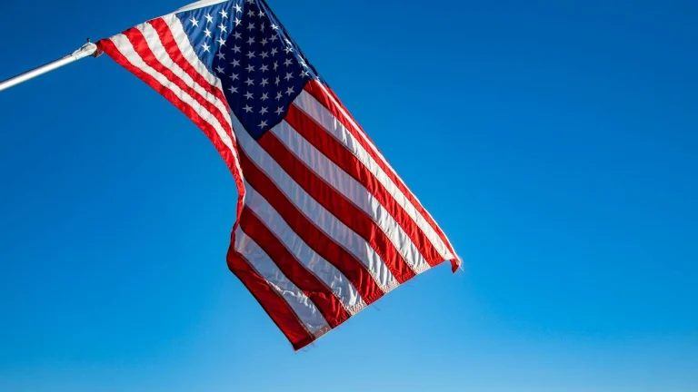 The American flag proudly waves on a flagpole against a clear blue sky, symbolizing freedom and patriotism.