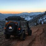 a jeep driving down a dirt road with mountains in the background