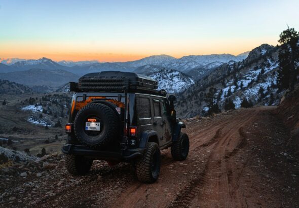 a jeep driving down a dirt road with mountains in the background