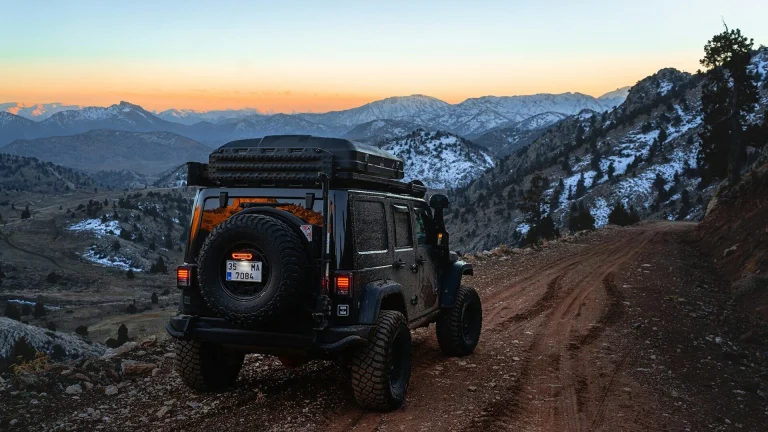 a jeep driving down a dirt road with mountains in the background