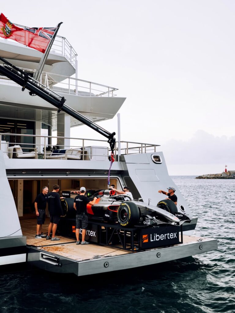 Formula 1 car being loaded onto a luxury superyacht in Monaco harbor during Grand Prix week