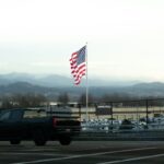 American flag waves near a dark truck and mountains.