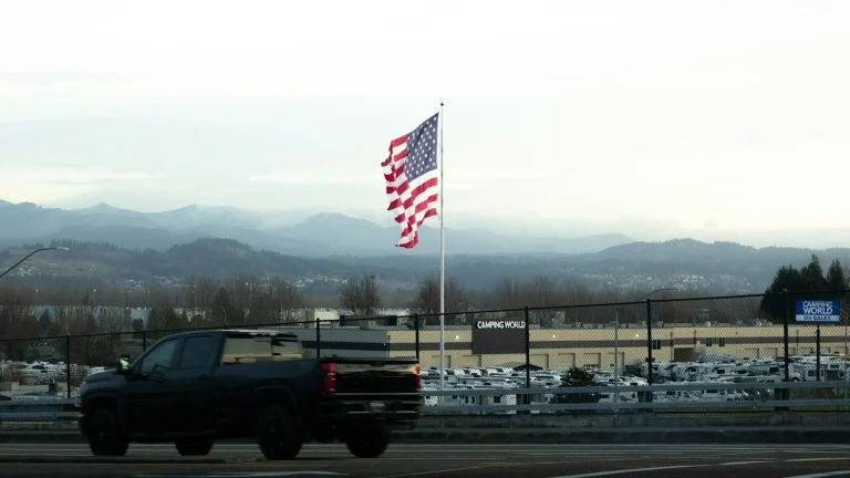 American flag waves near a dark truck and mountains.