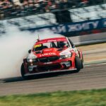 a red car driving down a race track with a lot of smoke coming out of