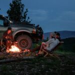 man in white shirt sitting on brown wooden chair near black suv during night time
