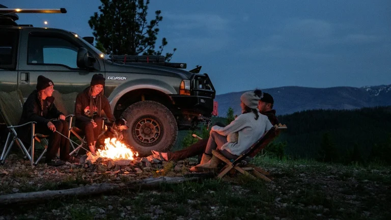 man in white shirt sitting on brown wooden chair near black suv during night time