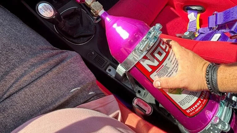 Hand holding pink nos bottle in car