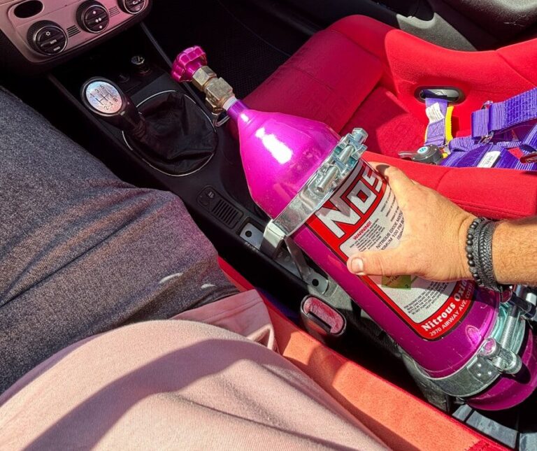Hand holding pink nos bottle in car