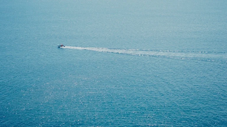 A boat leaves a white wake on the blue ocean.