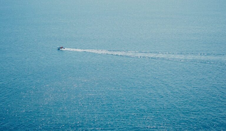 A boat leaves a white wake on the blue ocean.