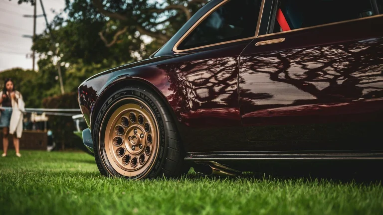 Close-up of a vintage burgundy car on grass.