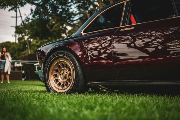 Close-up of a vintage burgundy car on grass.