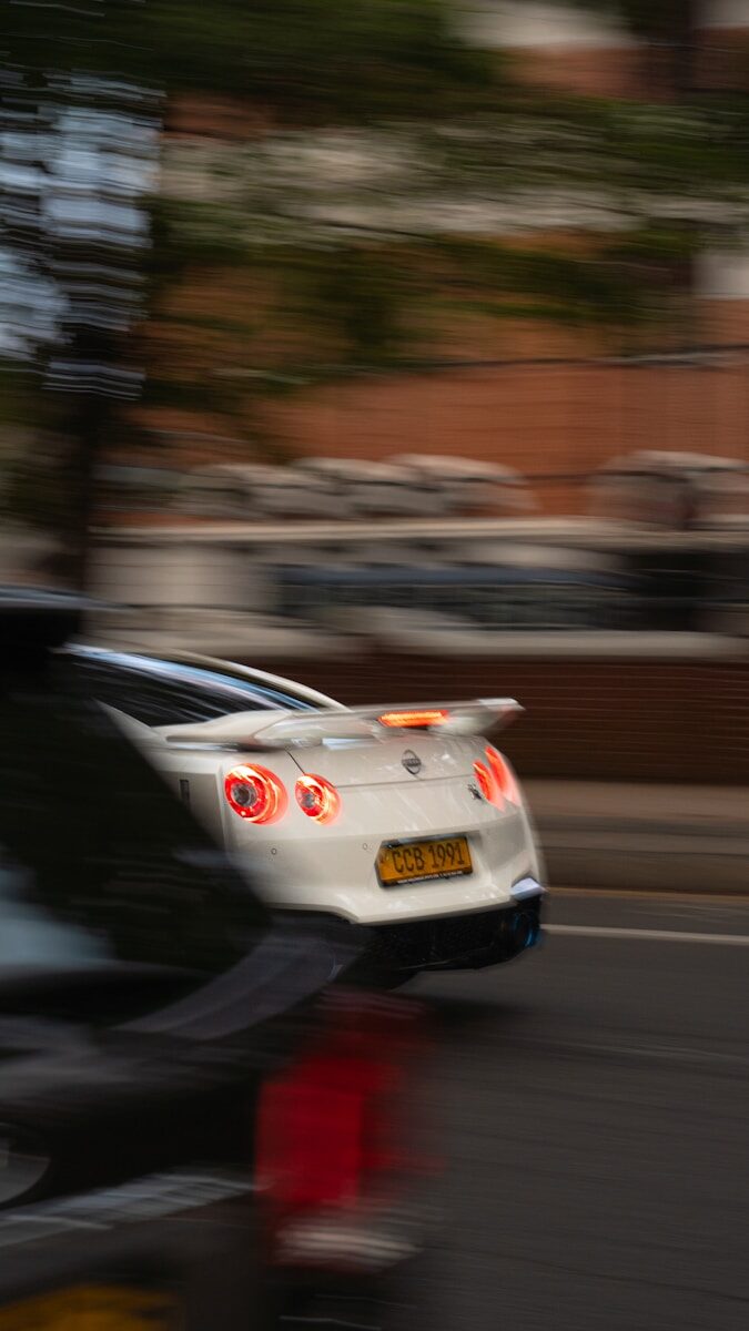 White sports car with glowing taillights in motion.