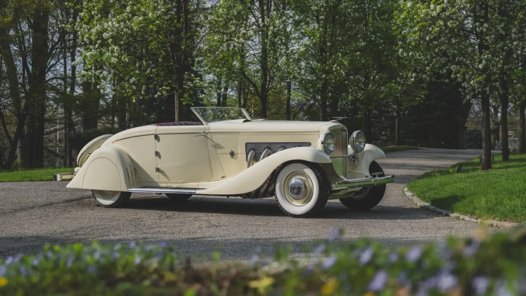 Cream-colored prewar Delage roadster with flowing fenders parked on a gravel drive