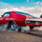 red chevrolet camaro on gray asphalt road under blue and white sunny cloudy sky during daytime