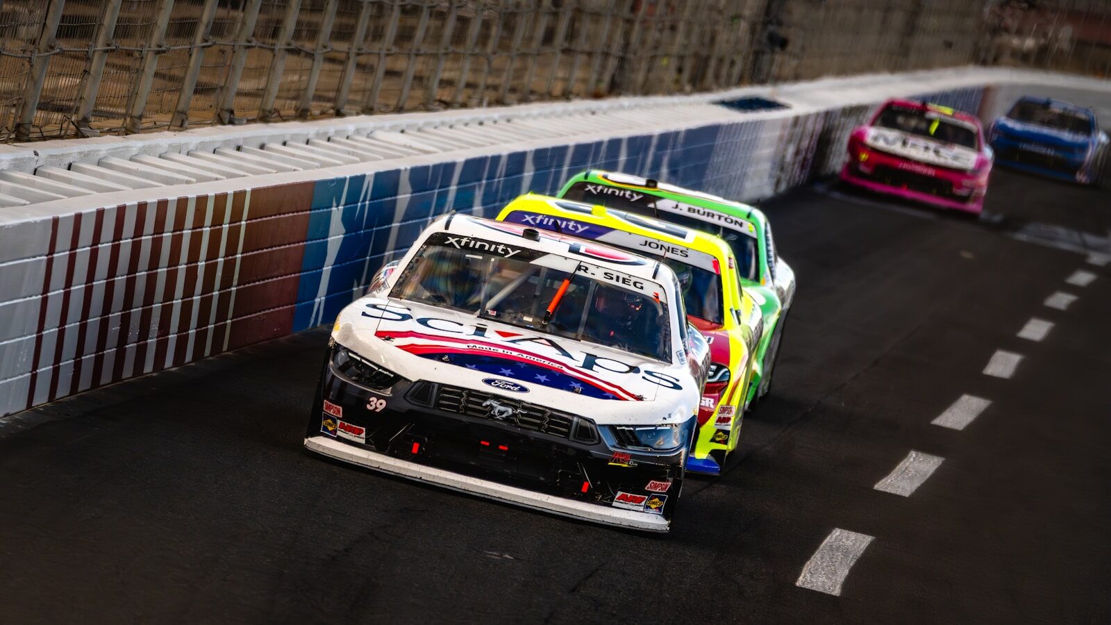 Race cars speed around a banked turn on a track.
