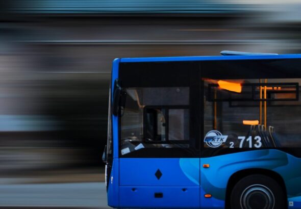 a blue bus driving down a street next to a tall building