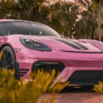 a pink sports car parked in front of some trees