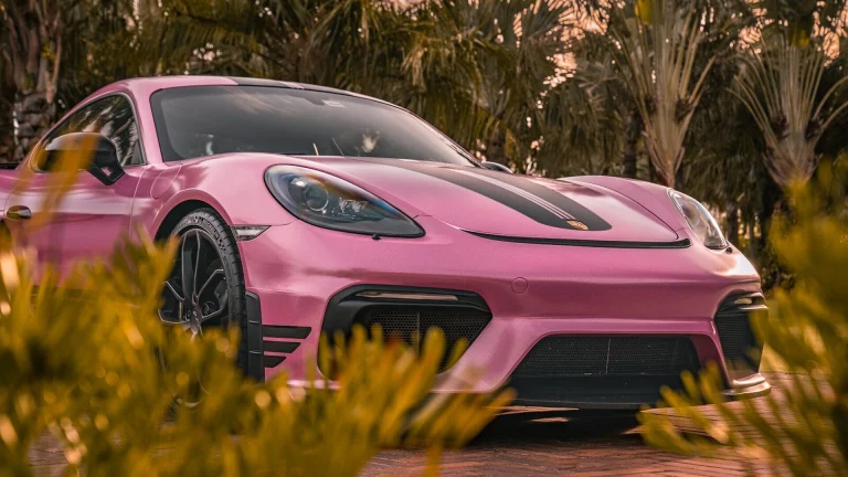 a pink sports car parked in front of some trees