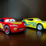 two red and yellow Disney Cars plastic toys on brown wooden surface