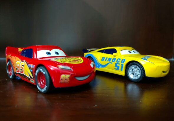 two red and yellow Disney Cars plastic toys on brown wooden surface