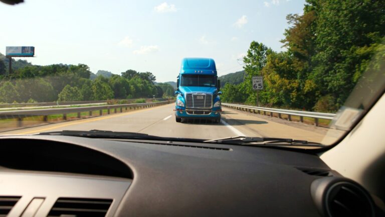 Blue semi-truck approaching on a highway from a car's perspective.
