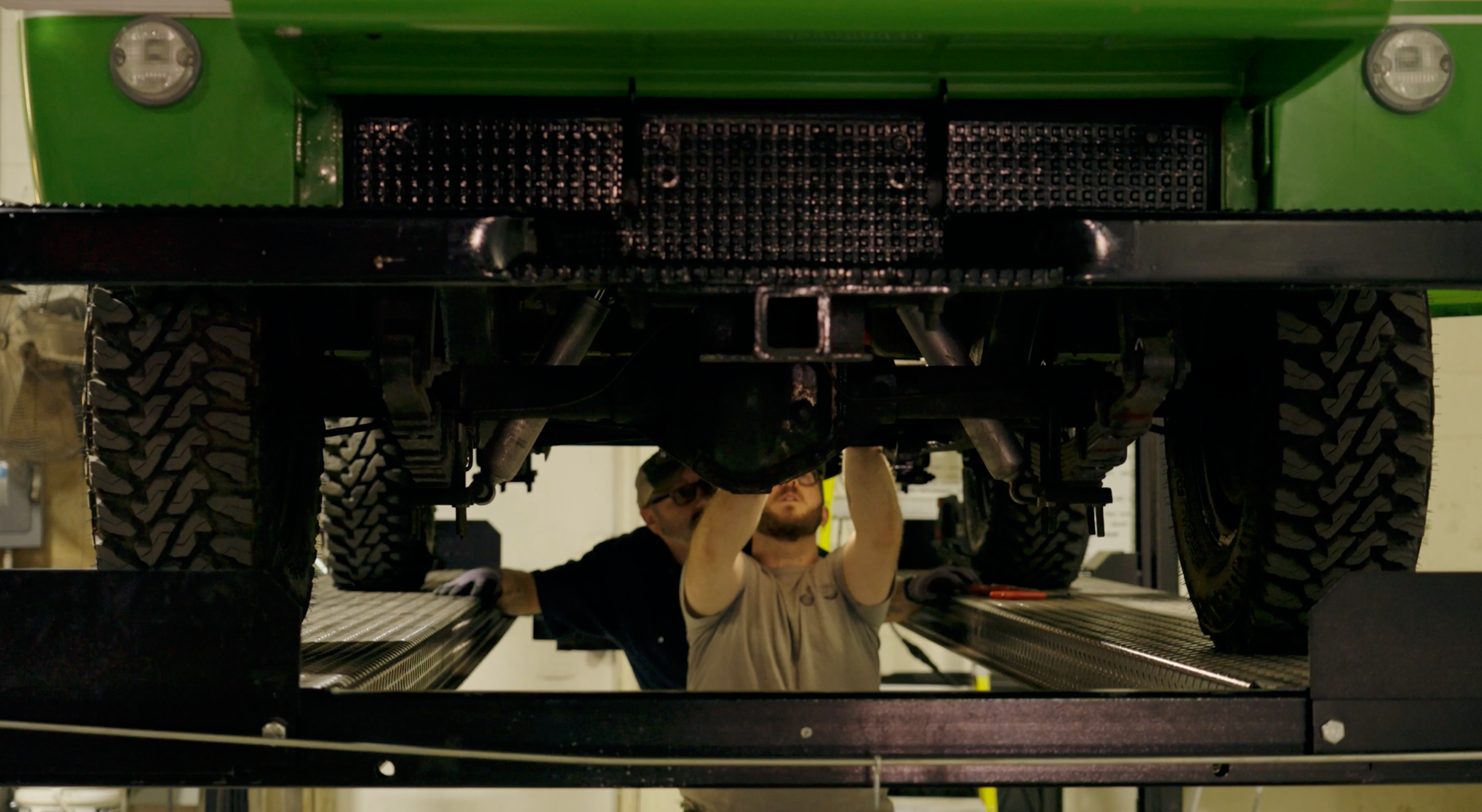 Technicians working under the 1970 Scout 800A EV conversion on a lift