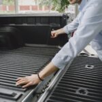 A man in a blue shirt opens the bed of a truck in a brightly lit indoor space.
