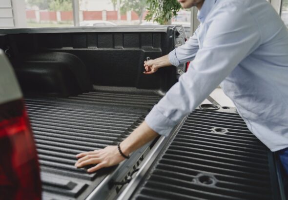 A man in a blue shirt opens the bed of a truck in a brightly lit indoor space.