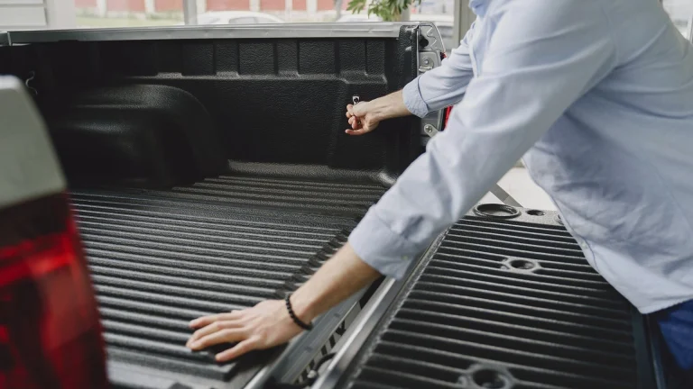 A man in a blue shirt opens the bed of a truck in a brightly lit indoor space.