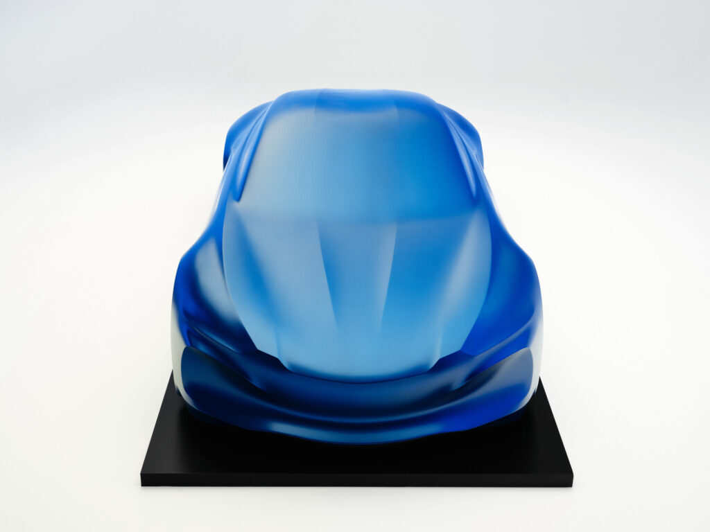 Front view of the blue draped Alpine A110 sculpture on a black plinth