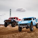 Off-road race truck launching over a desert rise in a cloud of dust during a Baja desert race