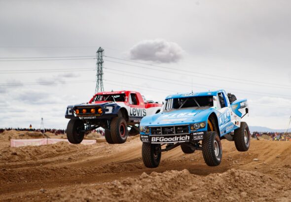Off-road race truck launching over a desert rise in a cloud of dust during a Baja desert race