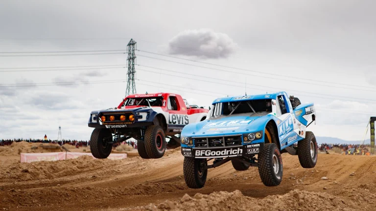 Off-road race truck launching over a desert rise in a cloud of dust during a Baja desert race