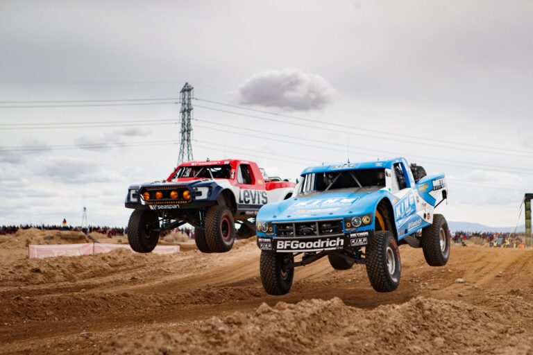 Off-road race truck launching over a desert rise in a cloud of dust during a Baja desert race