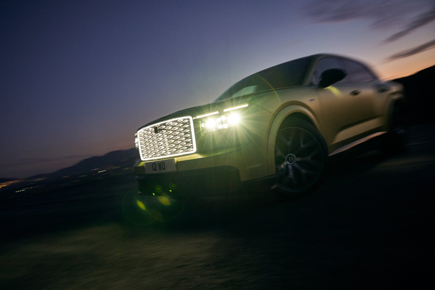 Bentley Torcal driving at dusk with its illuminated diamond grille and headlights on