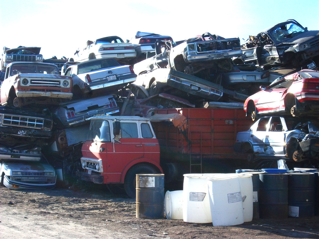Cars and pickup trucks stacked in a pile at a scrap yard awaiting shredding