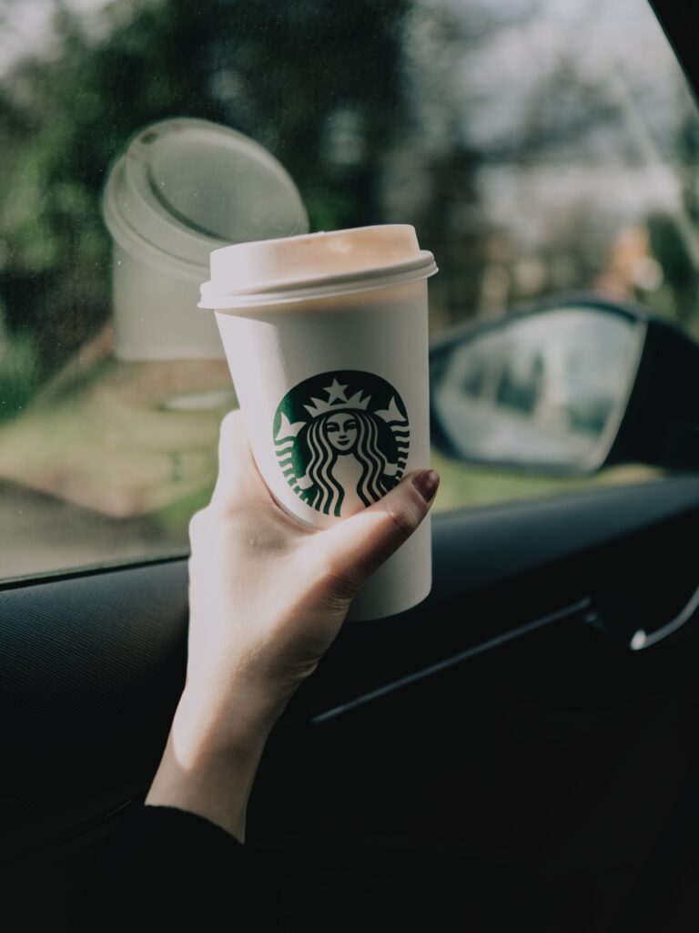 Hand holding a to-go coffee cup inside a car during a morning commute