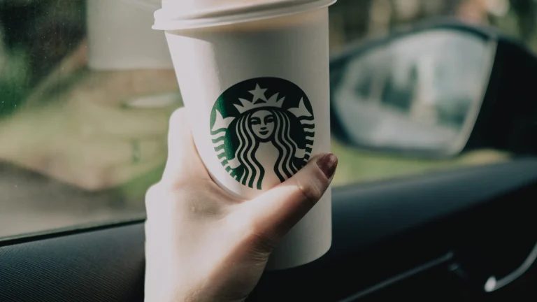 Hand holding a to-go coffee cup inside a car during a morning commute