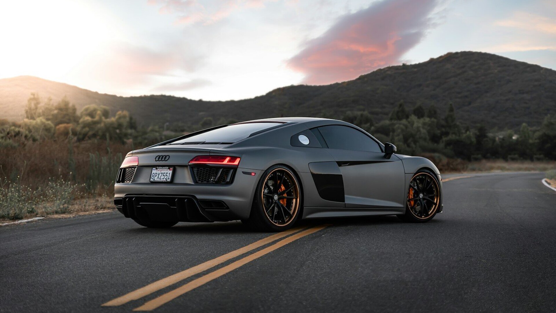 A matte grey Audi R8 sports car on a winding road at golden hour