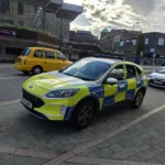 A yellow and blue Battenburg-liveried police car parked near Derby bus station