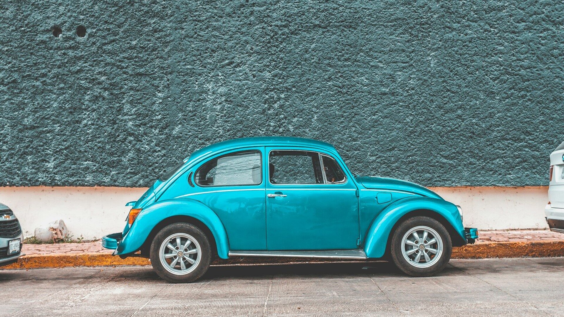 teal Volkswagen Beetle car parked beside sidewalk