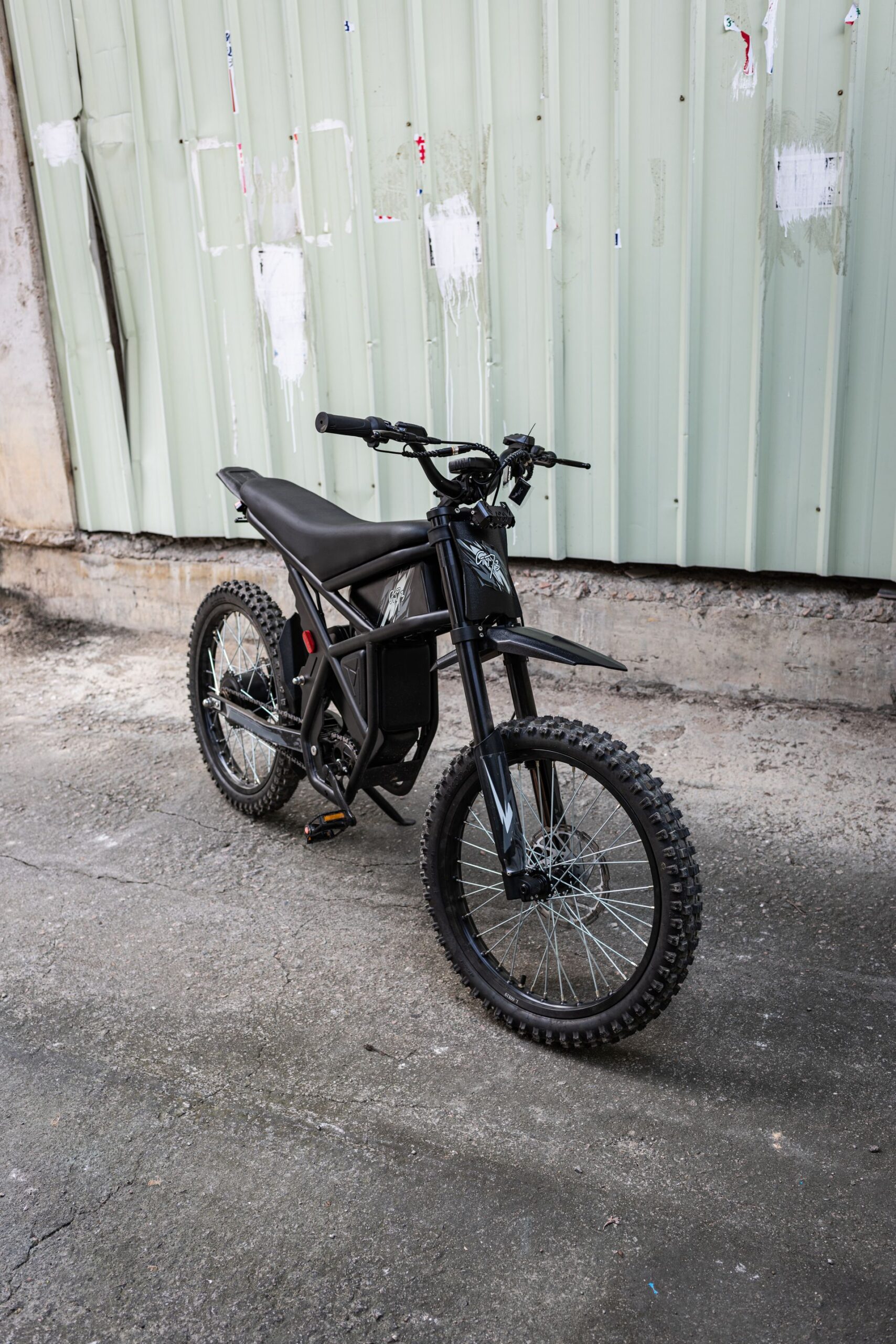 Electric dirt bike parked on pavement against a metal wall