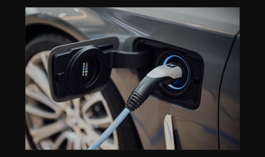Close-up of an electric vehicle charging connector plugged into a car, representing the Scout Traveler's electric powertrain