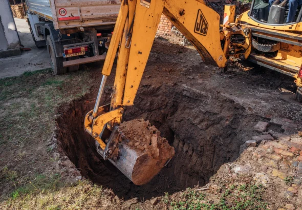 An excavator bucket digging a deep hole in dirt
