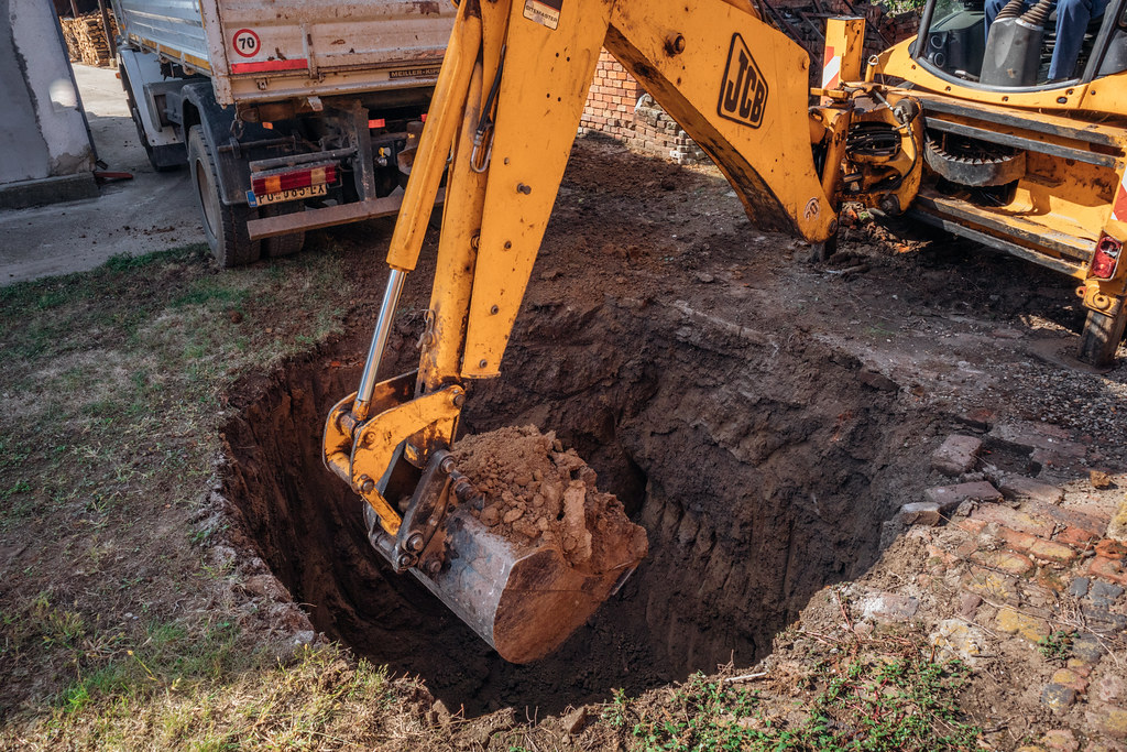 An excavator bucket digging a deep hole in dirt