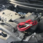 Red jumper clamps connected to a car battery in an engine bay