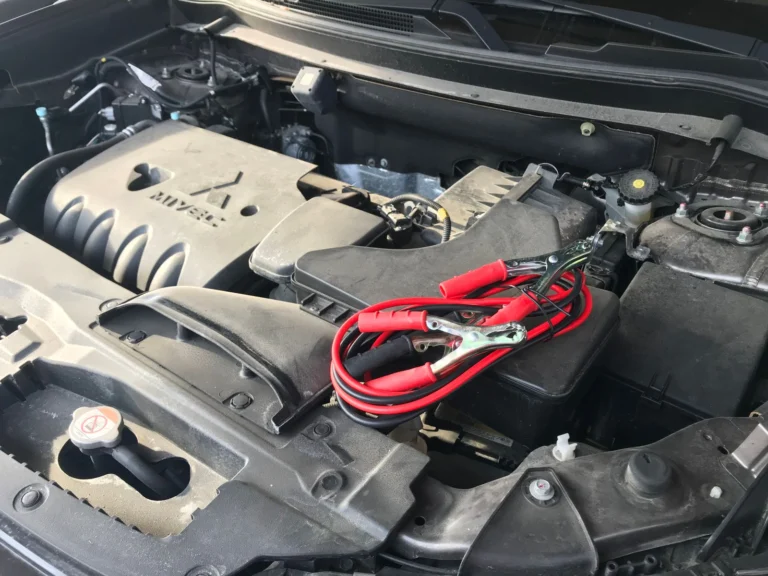Red jumper clamps connected to a car battery in an engine bay