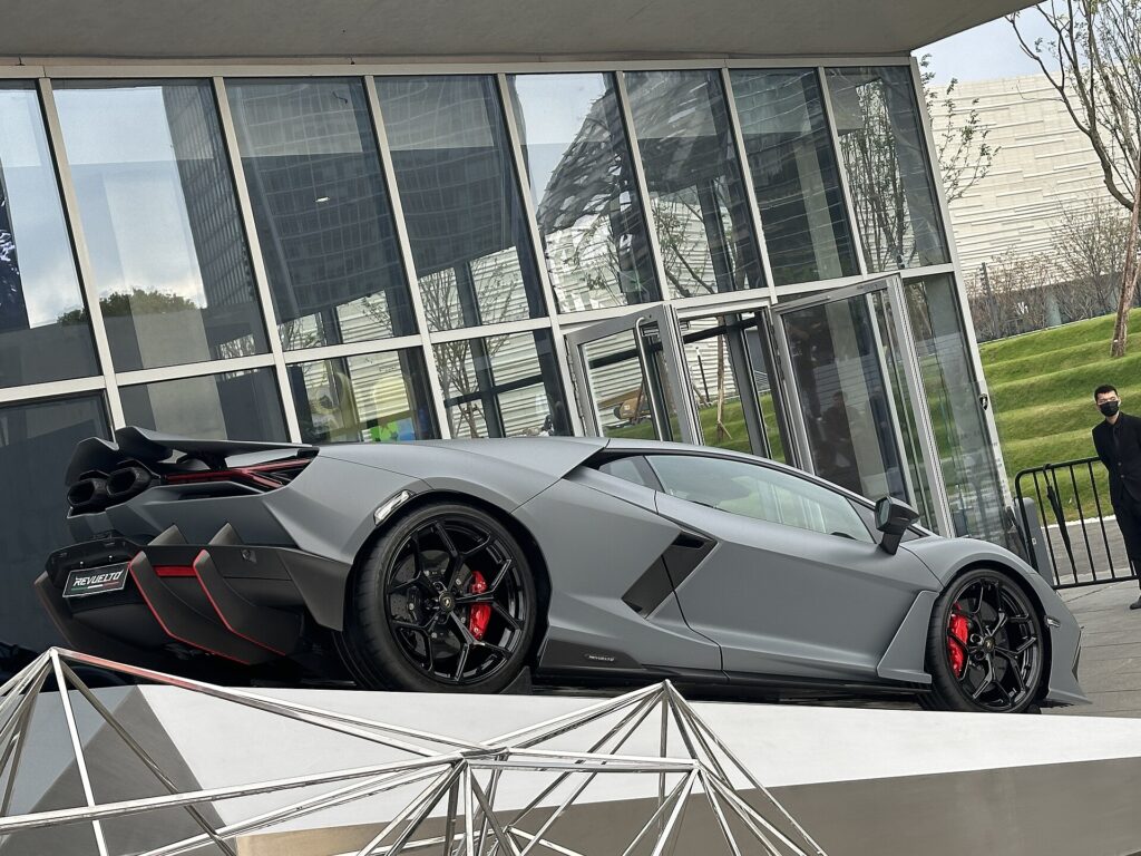 A grey stock Lamborghini Revuelto shown from the rear three-quarter, with its factory rear wing tucked into the tail